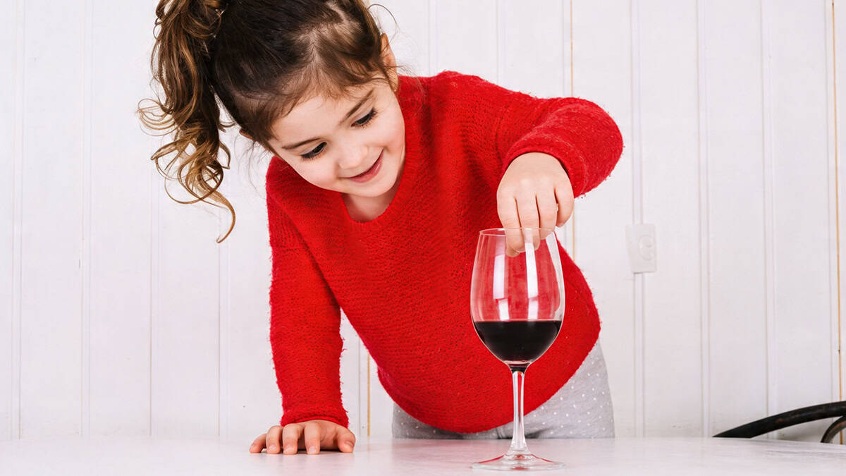 A little girl playing with a wine glass