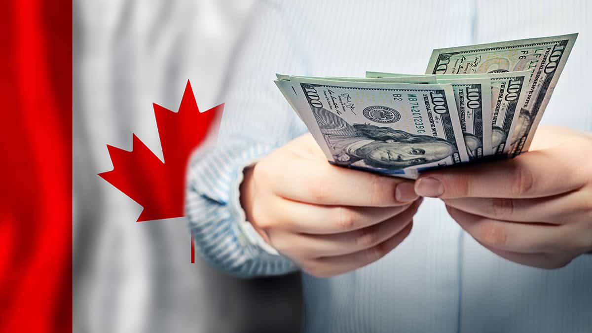 Person holding USD bills in front of a Canadian flag