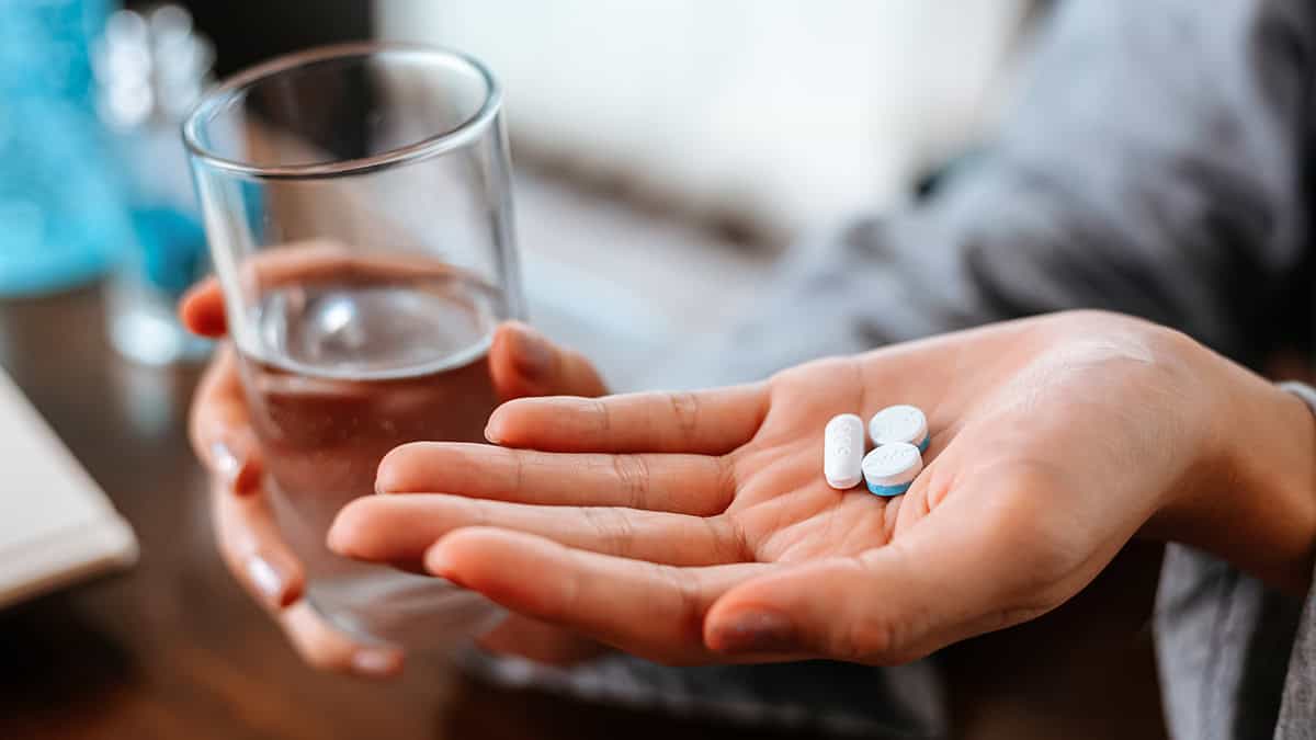Person holding a glass of water and two types of pills